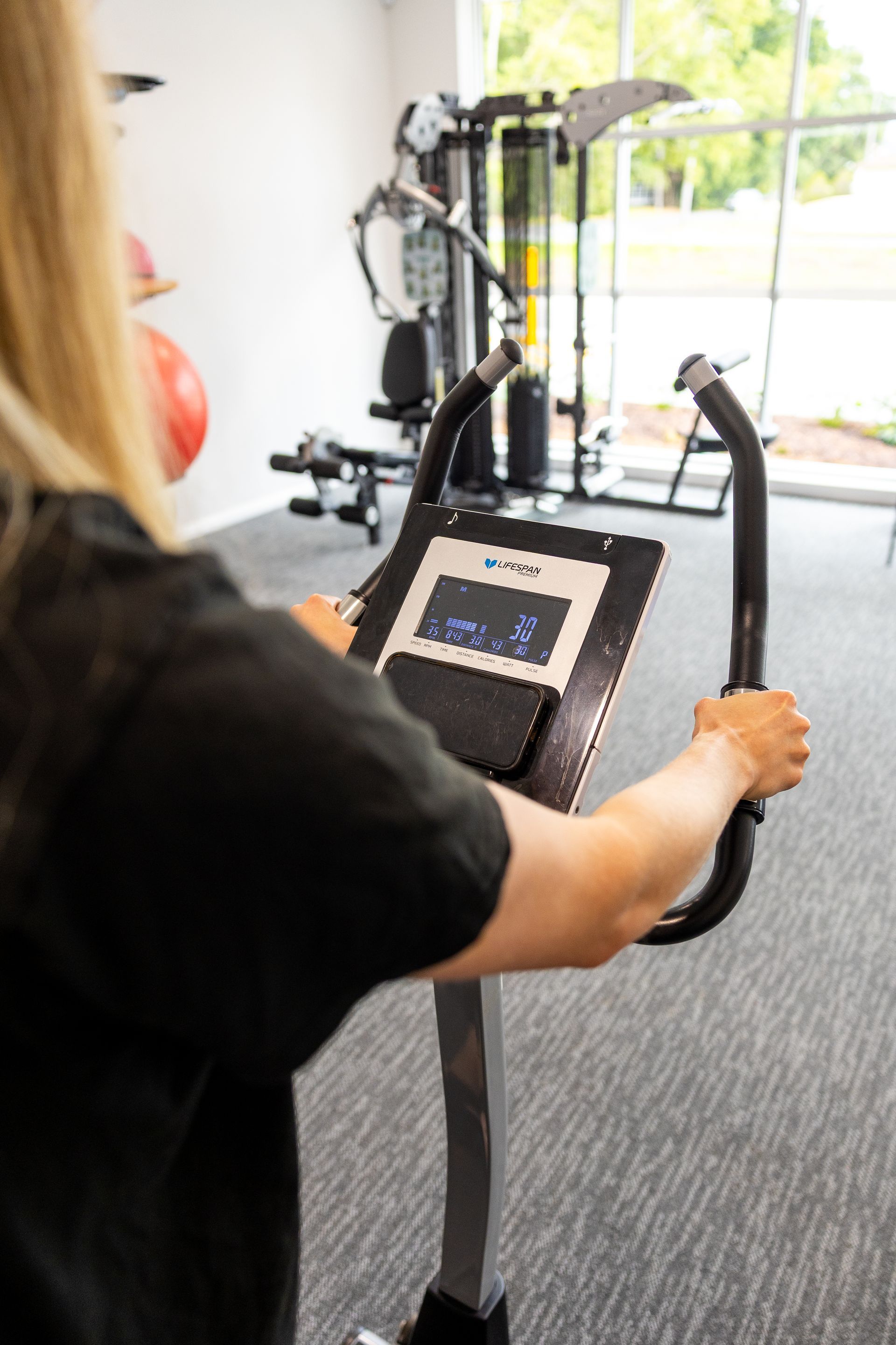 Person using a stationary bike with a touchscreen display in a bright gym room— Forerunner Physio In Taree, NSW