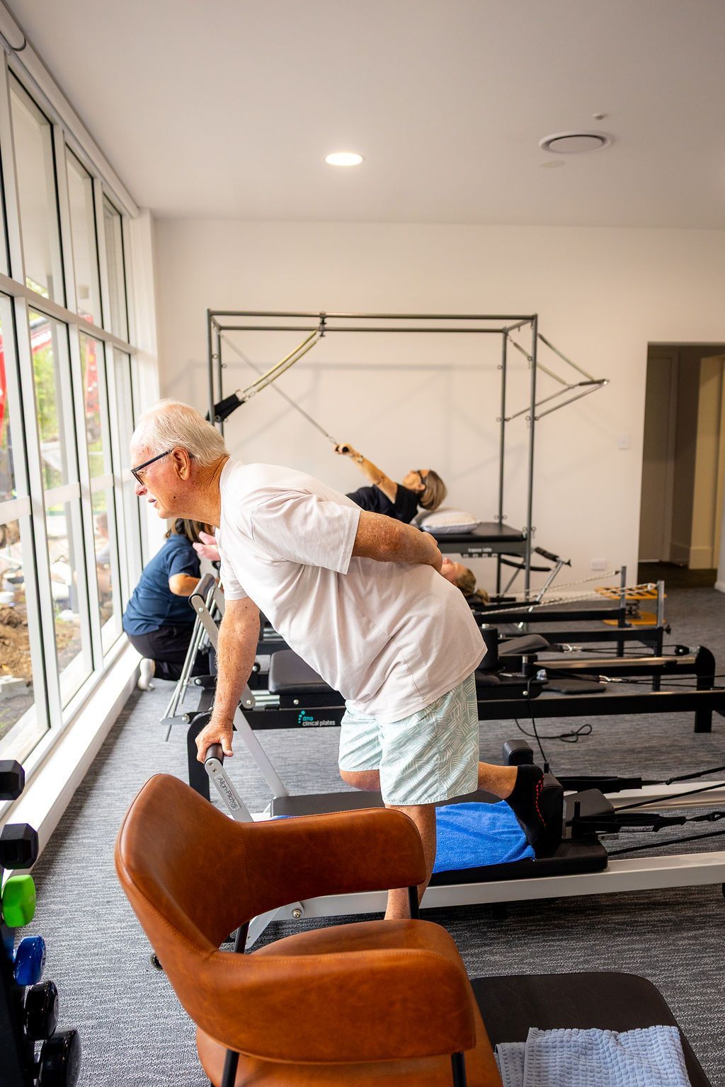 People exercising on Pilates reformers in a bright studio with large windows. — Forerunner Physio In Taree, NSW