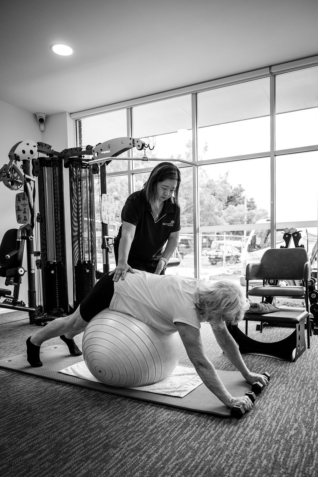Two people exercising in a gym, one balancing on a stability ball while the other spots behind. — Forerunner Physio In Taree, NSW