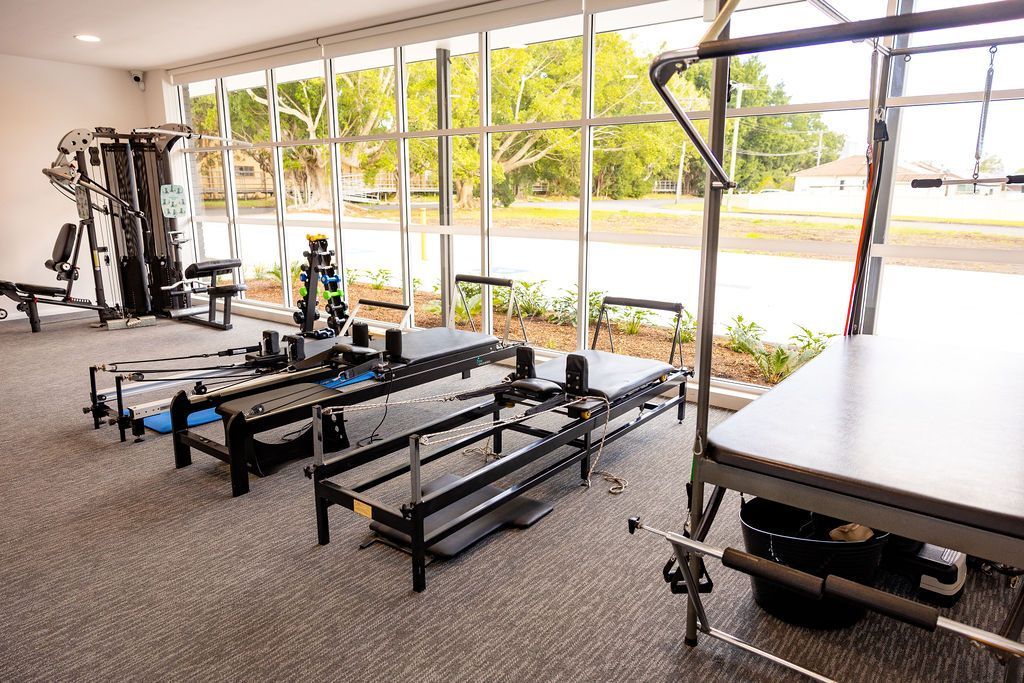 Indoor gym with weight machines, benches, and a bright windowed wall overlooking outdoors. — Forerunner Physio In Taree, NSW