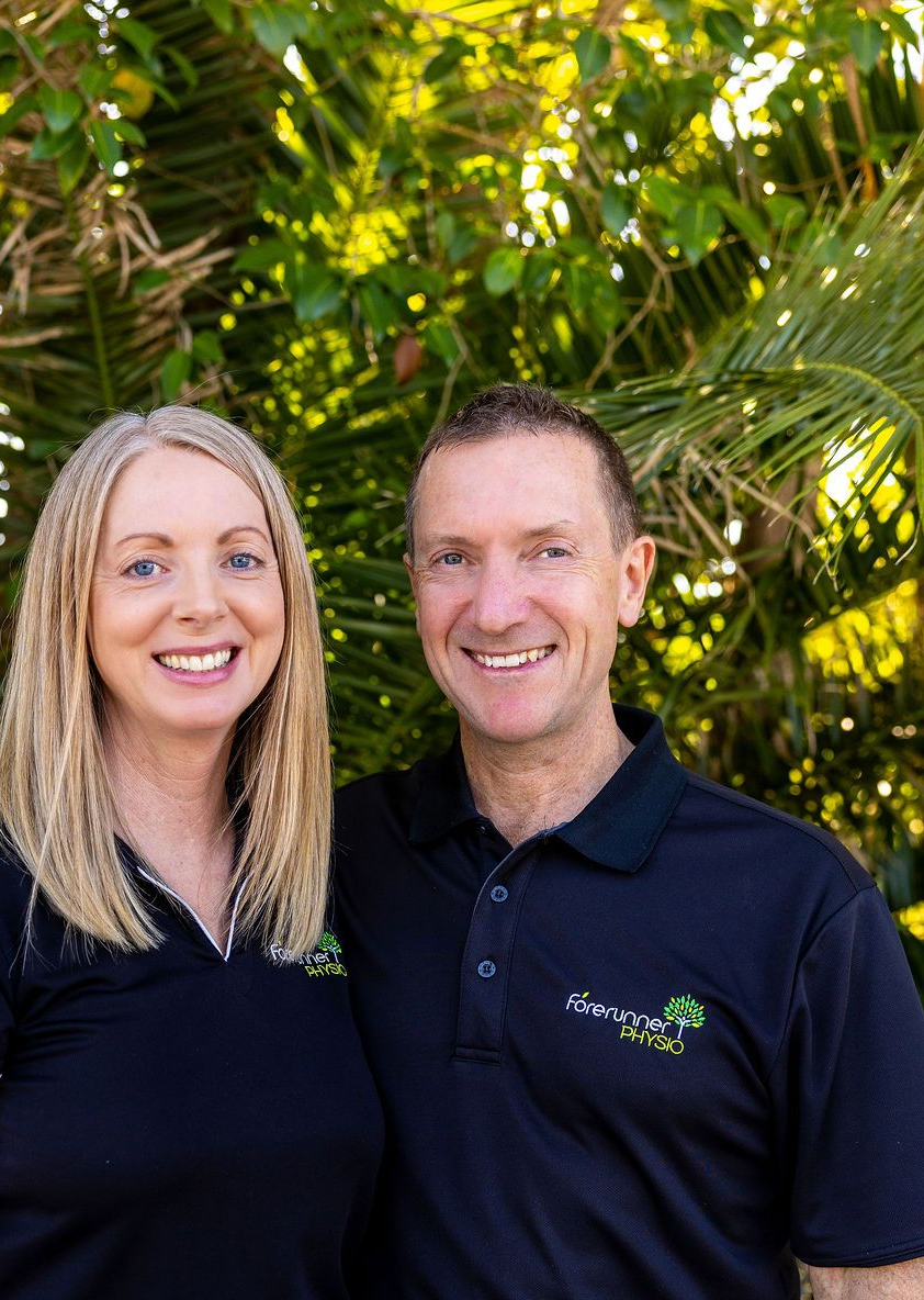 Two people in black shirts smiling outdoors in front of green foliage.— Forerunner Physio In Taree, NSW