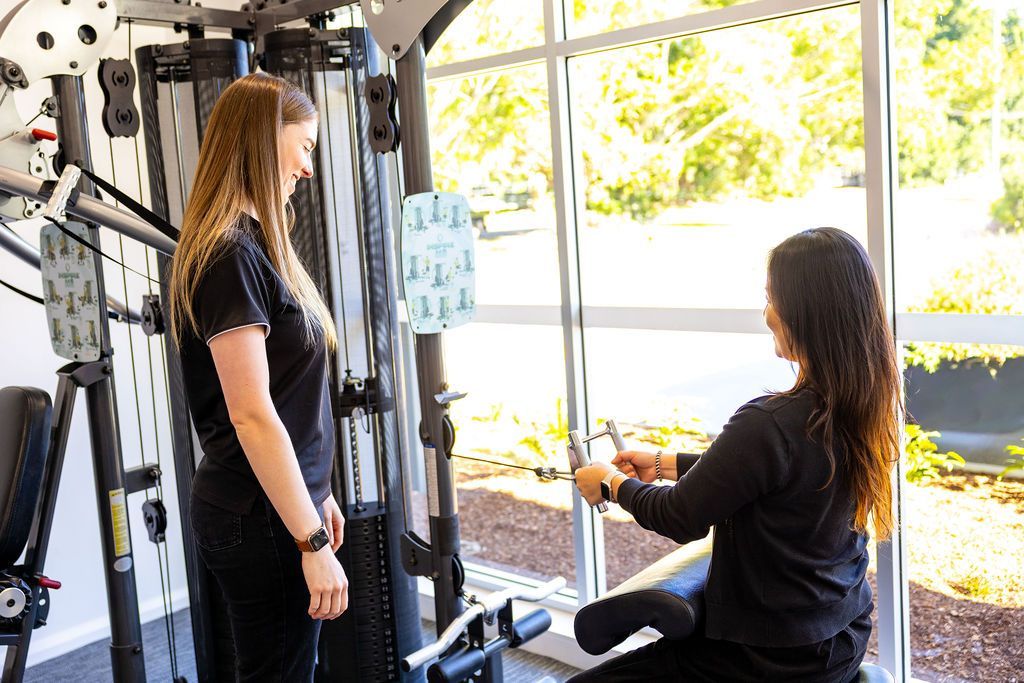 Two people using a cable machine in a bright gym with large windows. — Forerunner Physio In Taree, NSW