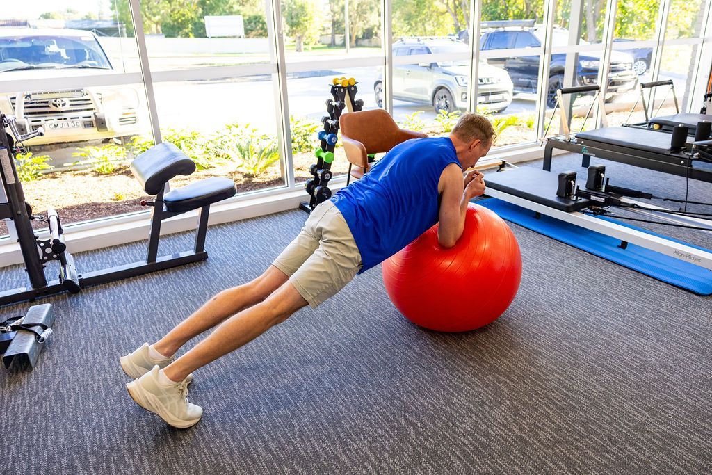 Person doing a plank on a red stability ball in a gym. — Forerunner Physio In Taree, NSW