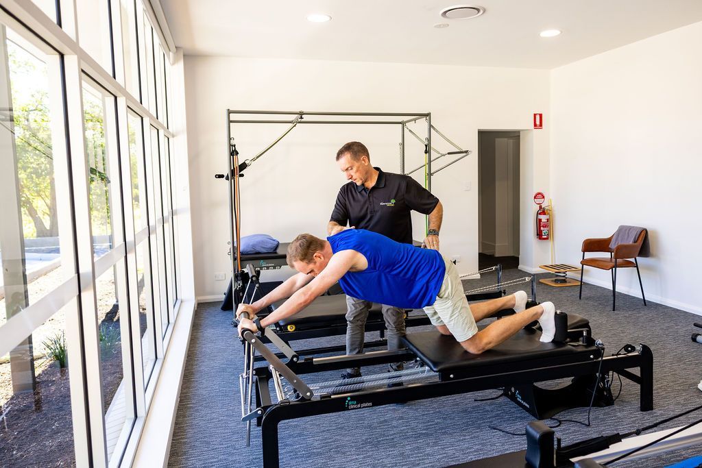 Man using a Pilates reformer while an instructor adjusts his form in a bright studio — Forerunner Physio In Taree, NSW