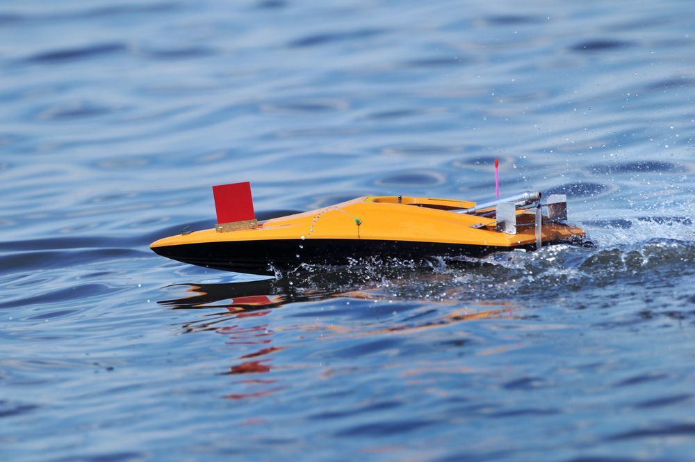 Yellow and black RC Boat On Blue Water, Red Flag On Top, Making A Wake — Midtown Hobbies In Lismore, NSW