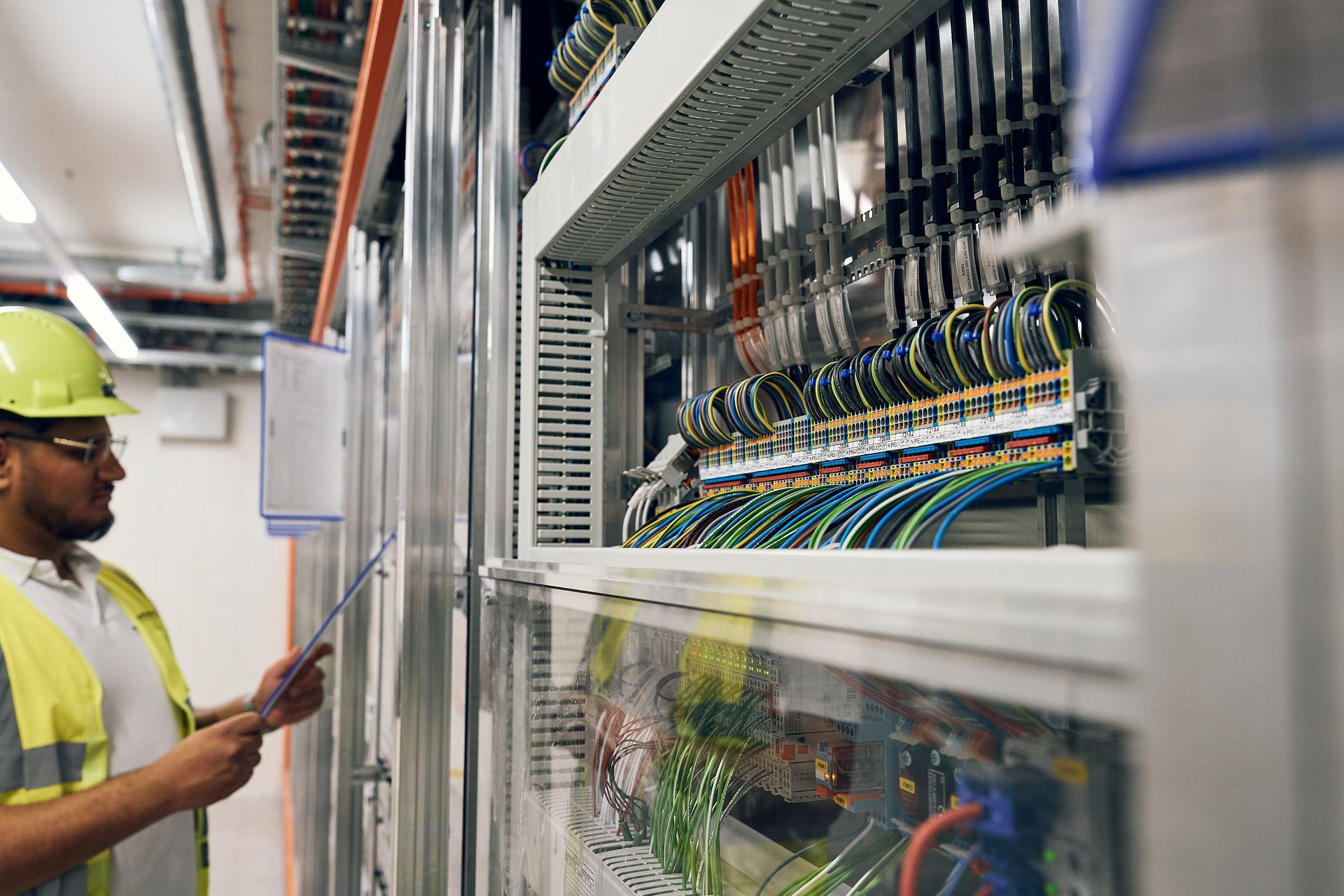 Ein Techniker in gelber Weste und Schutzhelm überprüft die elektrische Verkabelung in einem Serverraum.