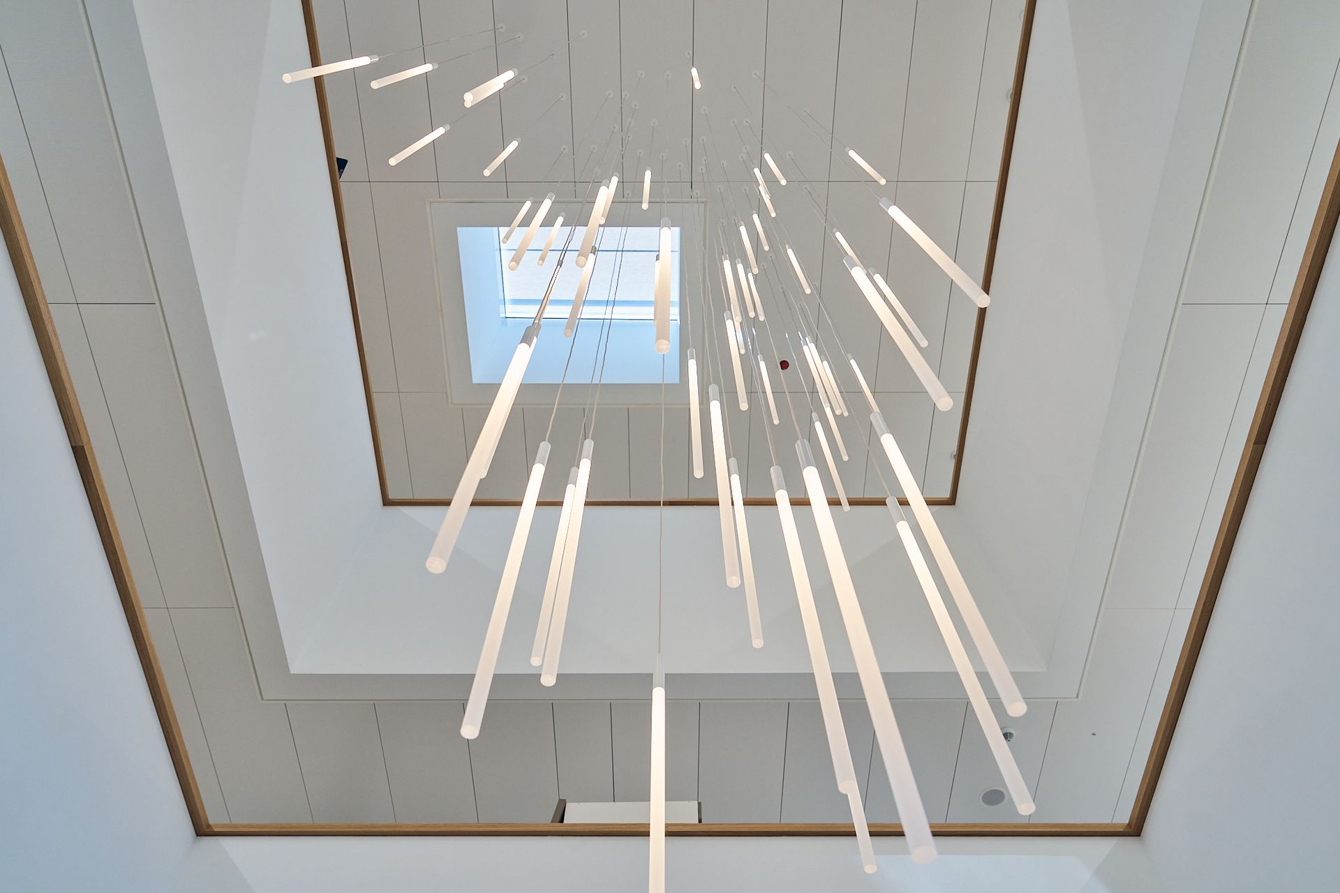 Decke mit quadratischem Oberlicht und vielen rechteckigen Hängeleuchten.
