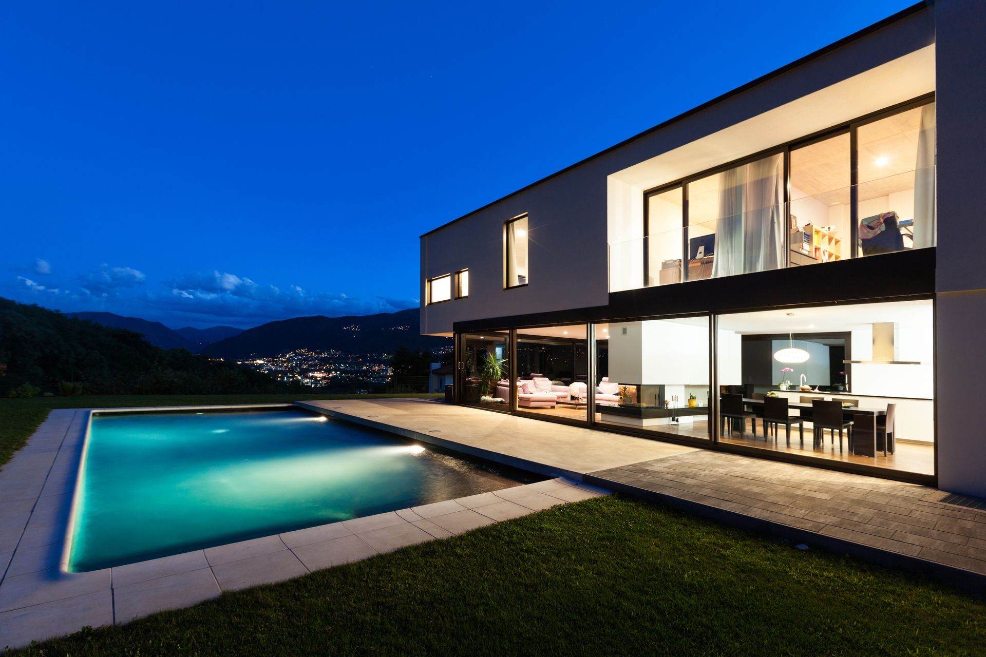 Modernes Haus mit nachts beleuchtetem Pool und Blick auf die Stadt.