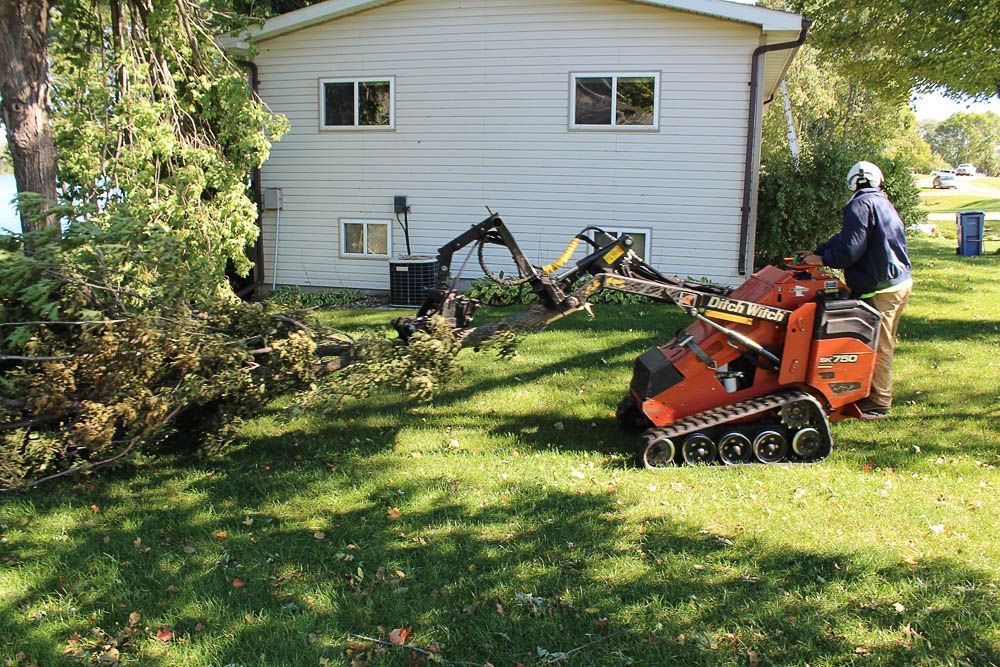 A man is using a tractor to dig a hole in the grass in front of a house.