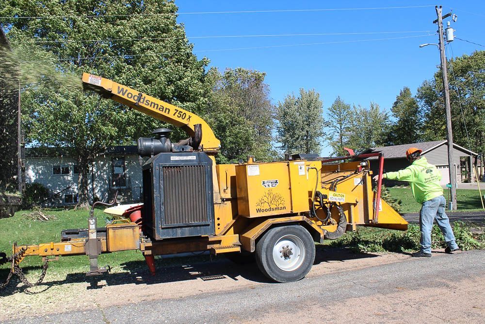 A man is standing next to a wood chipper on the side of the road.