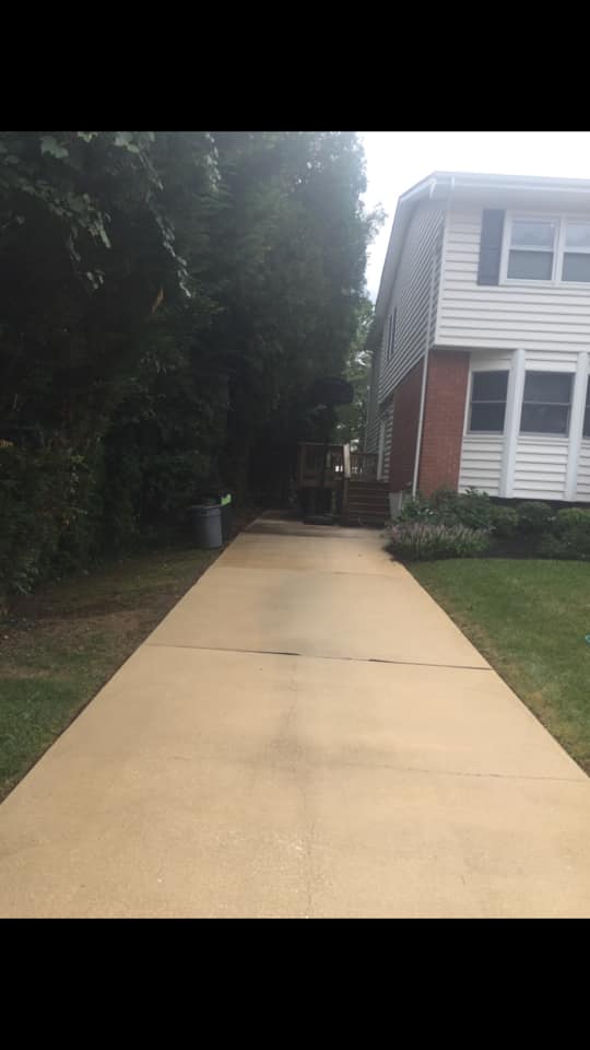 A concrete driveway leading to a house with trees on both sides.