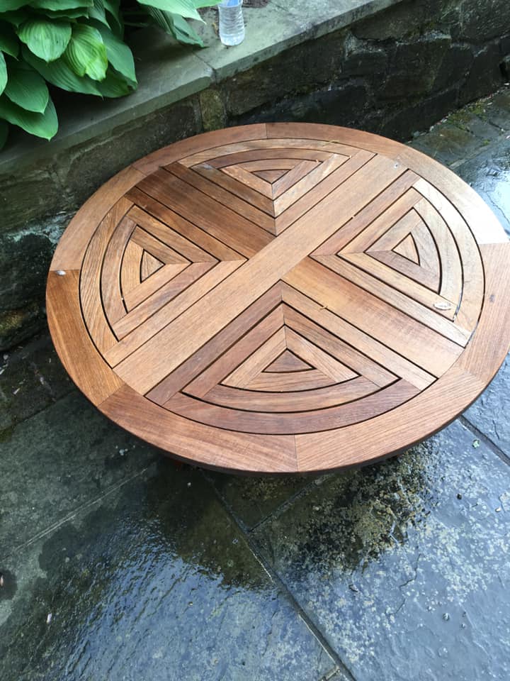 A wooden table with a geometric design on it is sitting on a concrete surface.