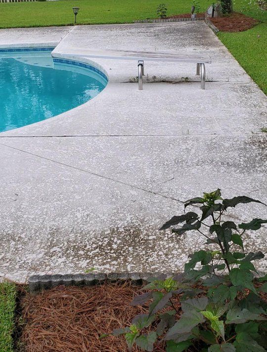 A concrete patio next to a swimming pool with a bench.