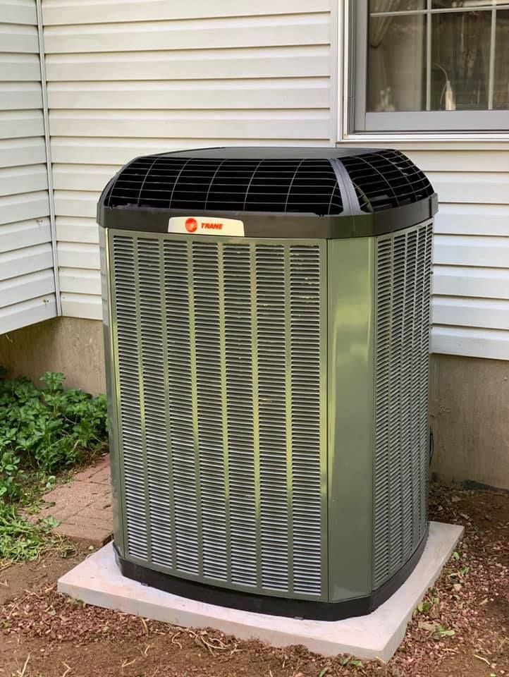 Air conditioner unit on concrete pad next to a house with beige siding and a window. Air conditioner unit on concrete pad next to a house with beige siding and a window.