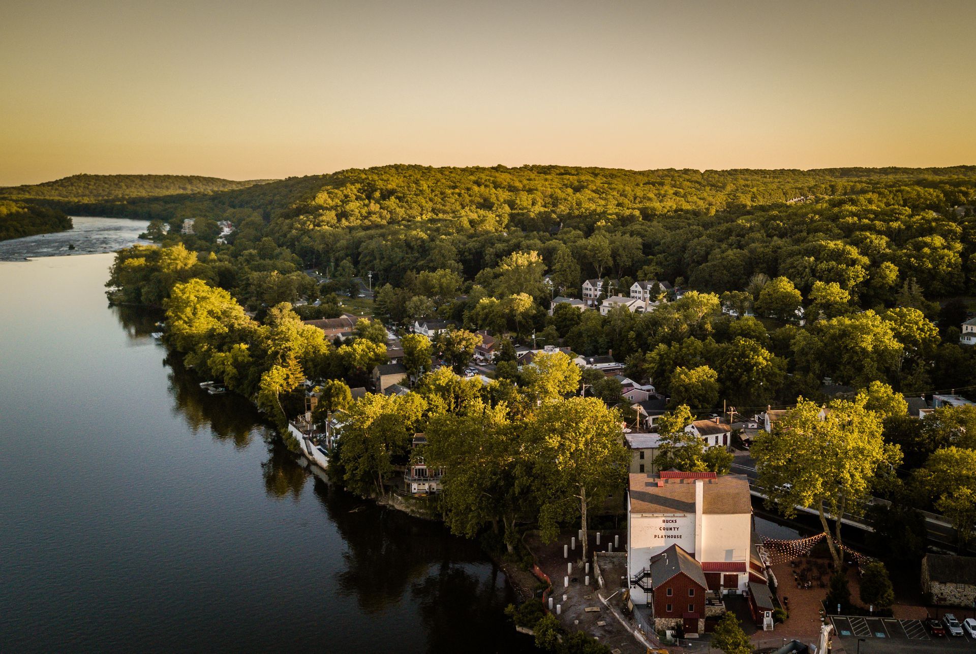 Aerial view of a riverfront town with lush green trees and buildings, at sunset. Aerial view of a riverfront town with lush green trees and buildings, at sunset.