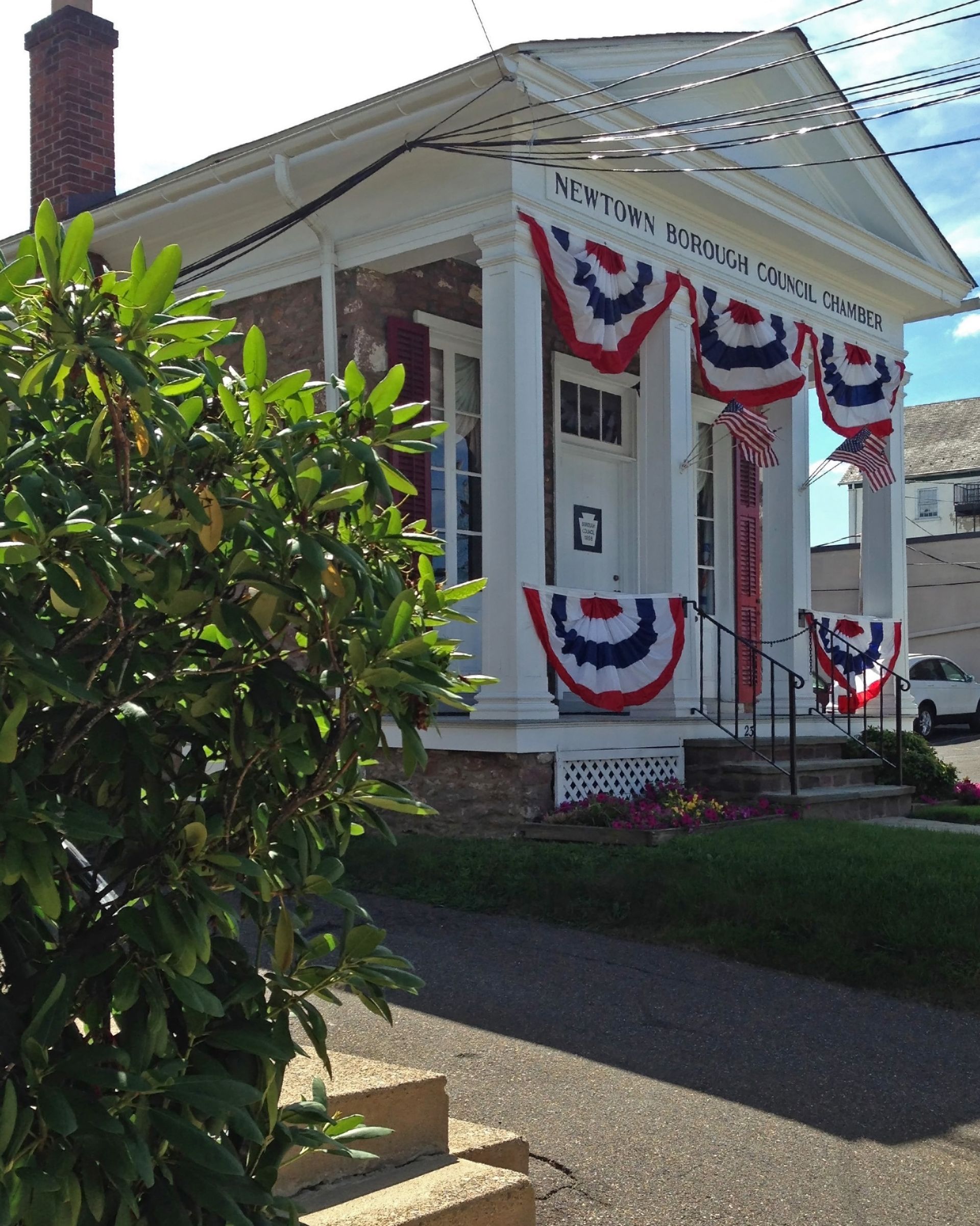 Small white building decorated with red, white, and blue bunting; a stone exterior and porch with pillars. Small white building decorated with red, white, and blue bunting; a stone exterior and porch with pillars.