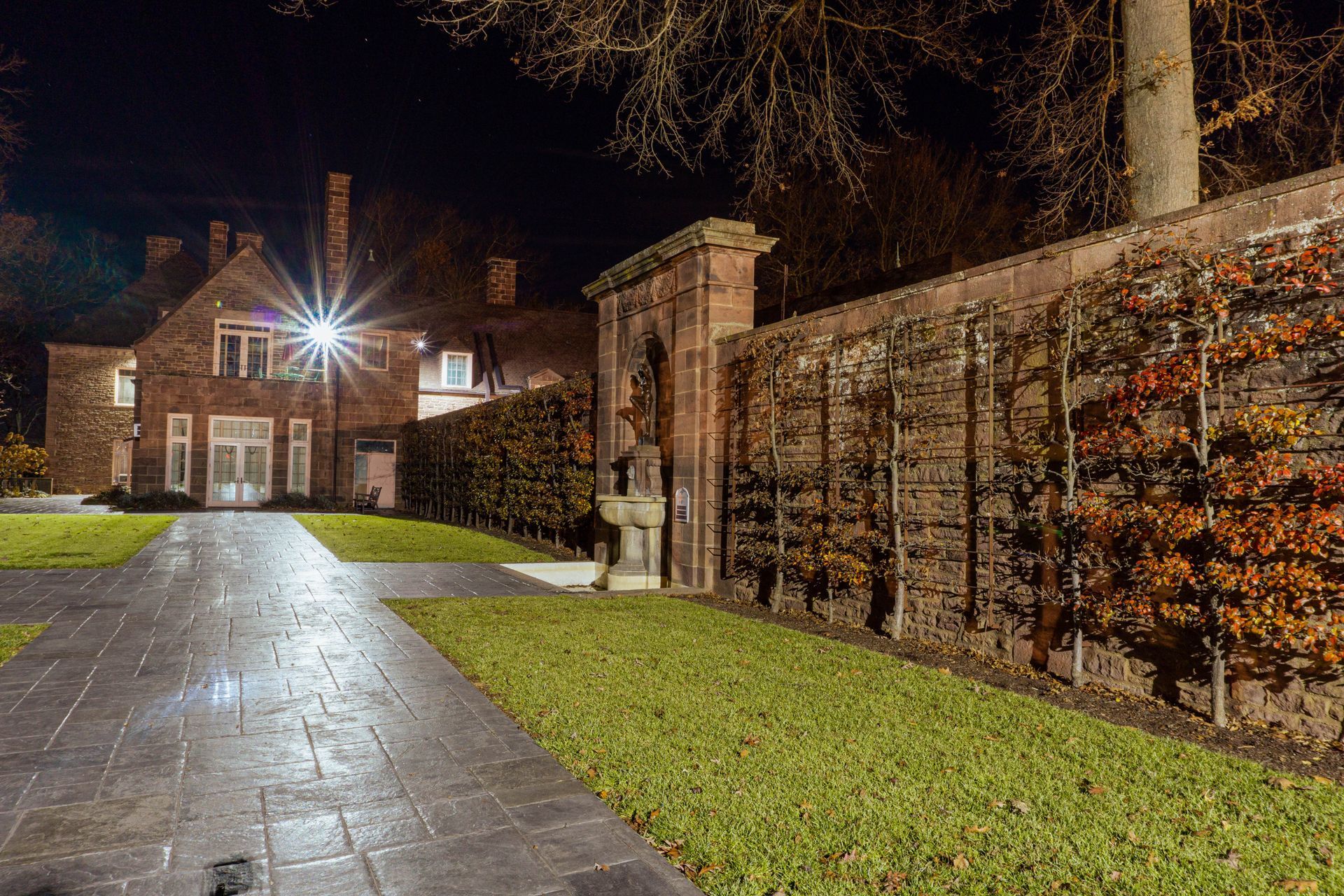 A brick house at night with a paved pathway, lit by a street lamp, and a hedge alongside the house. A brick house at night with a paved pathway, lit by a street lamp, and a hedge alongside the house.