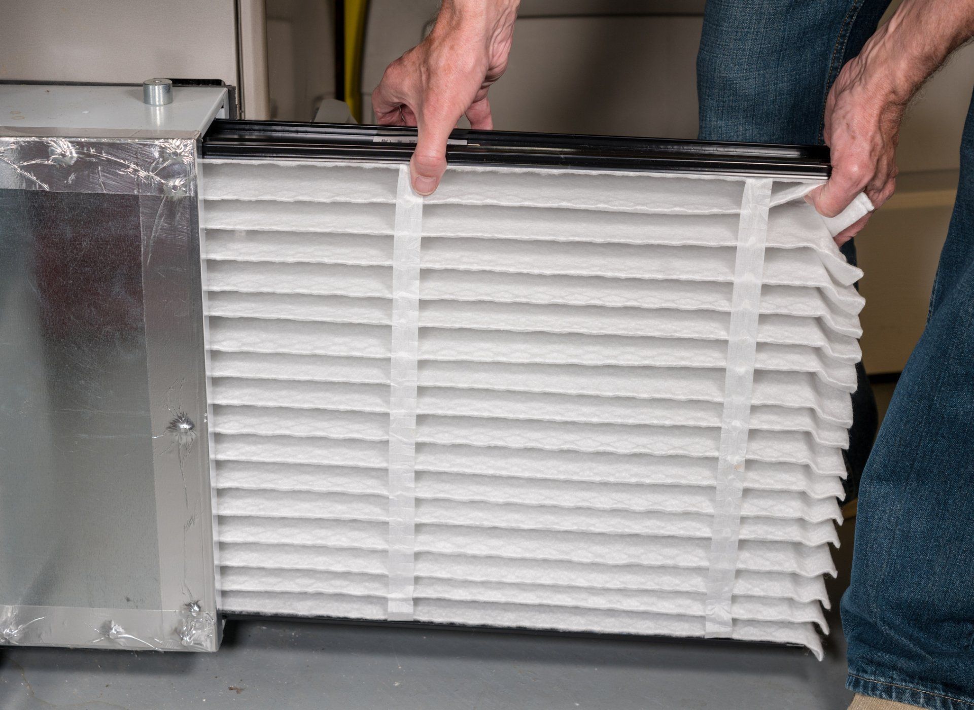 Person replacing an air filter in a furnace, filter is white, pleated, and square. Person replacing an air filter in a furnace, filter is white, pleated, and square.