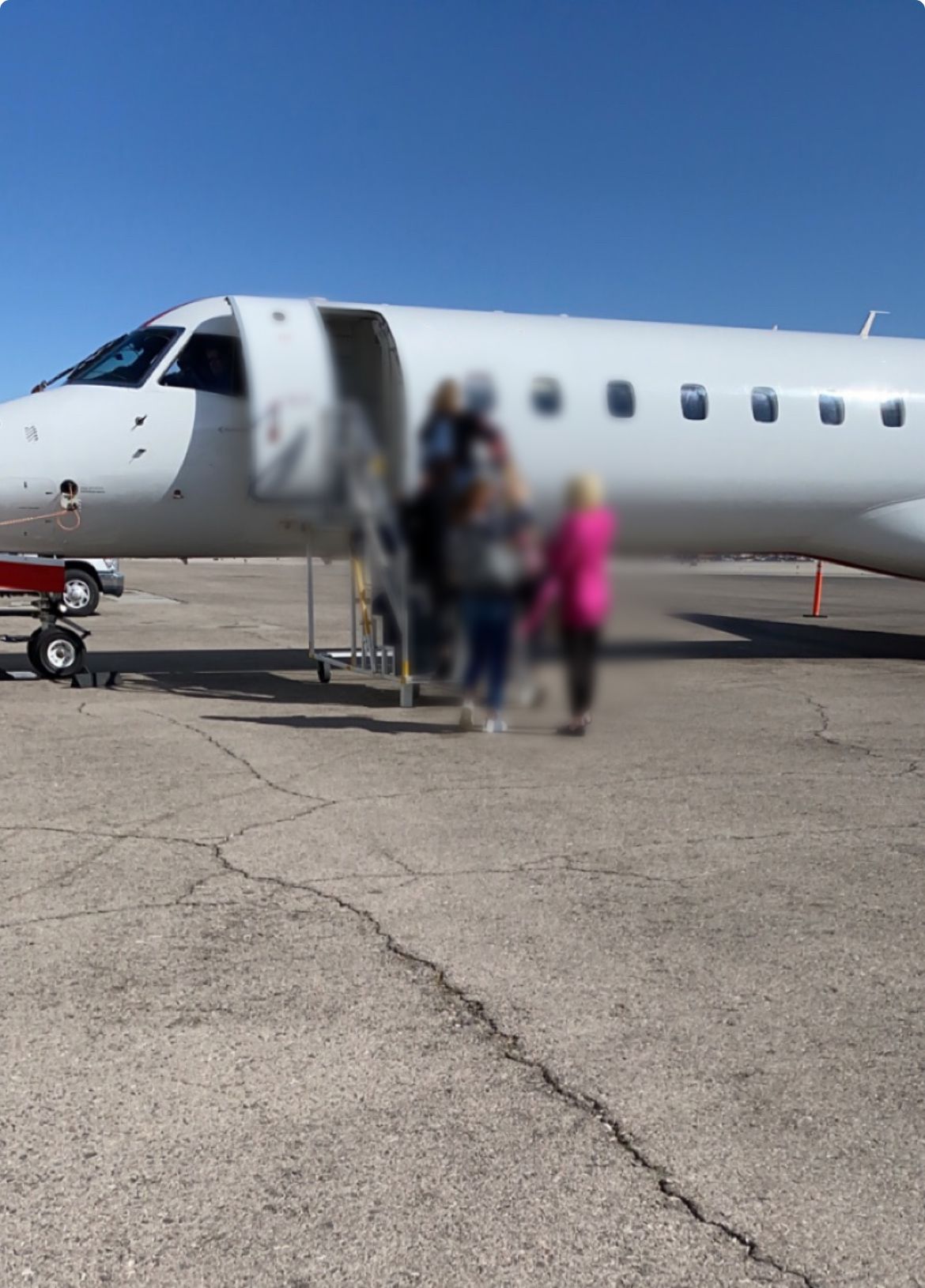 Passengers boarding a white airplane on a sunny day; pink jacket and blue jeans visible.