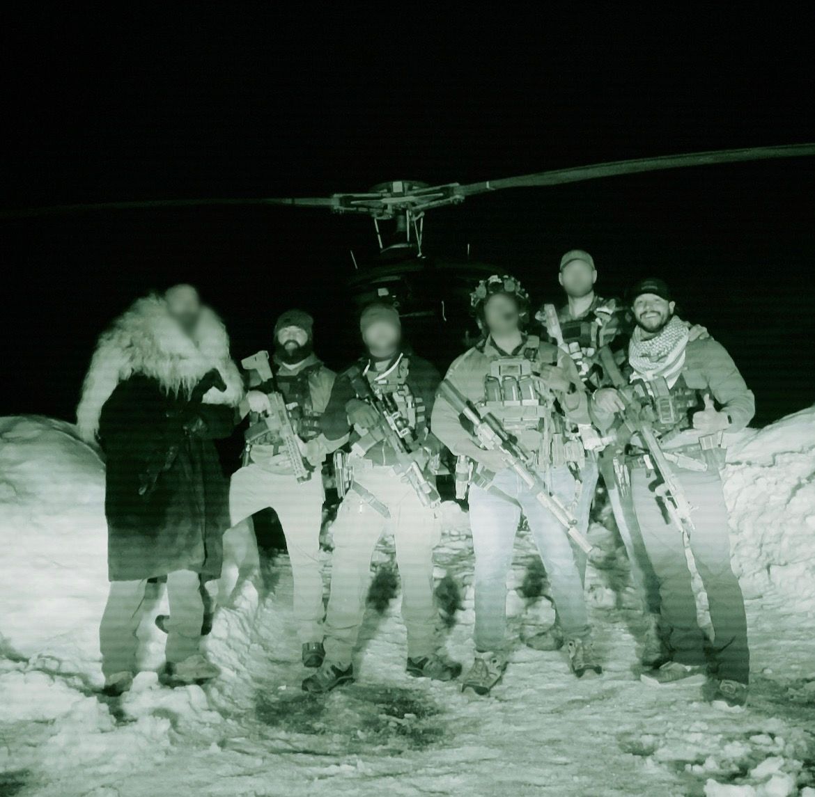 Night vision shot of armed soldiers in snowy landscape near a helicopter.
