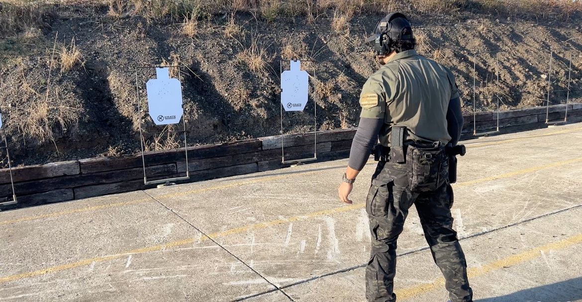 Man in tactical gear on a shooting range, facing targets.