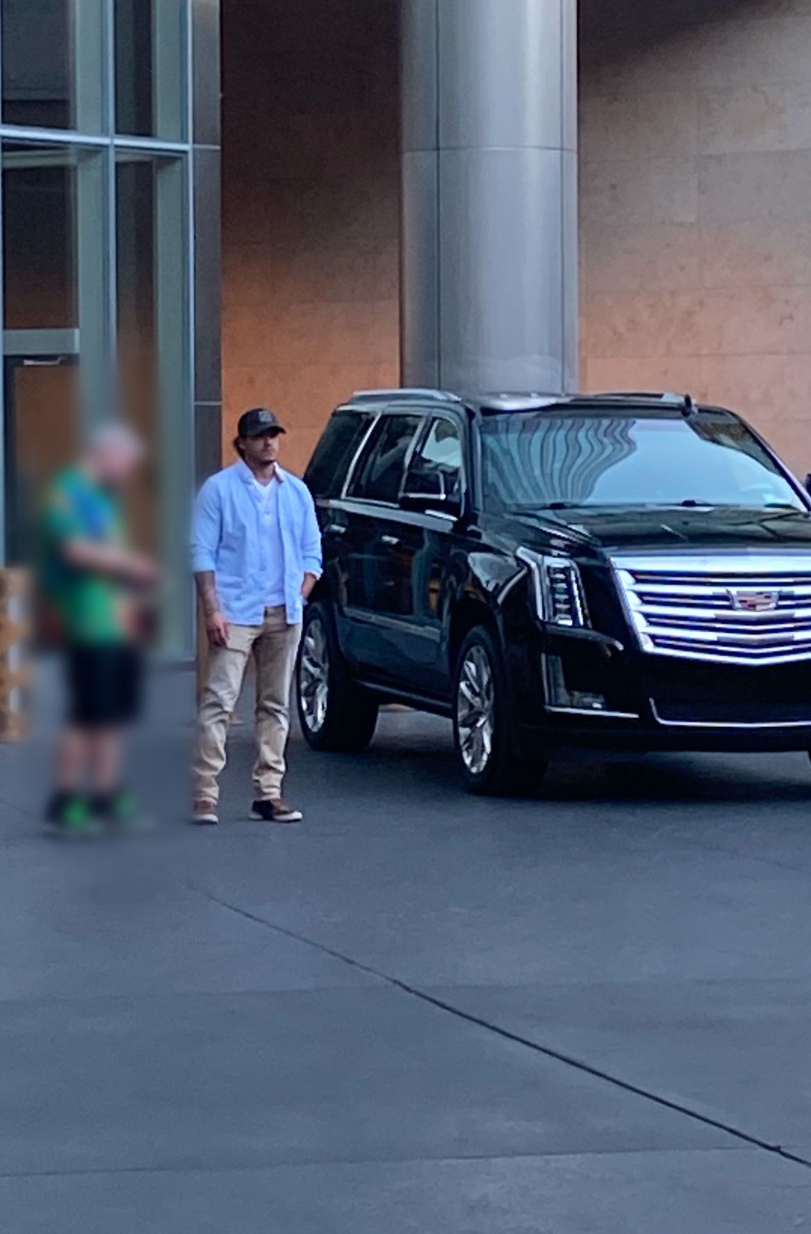 Man in light blue shirt and khakis standing next to black SUV outside a building.