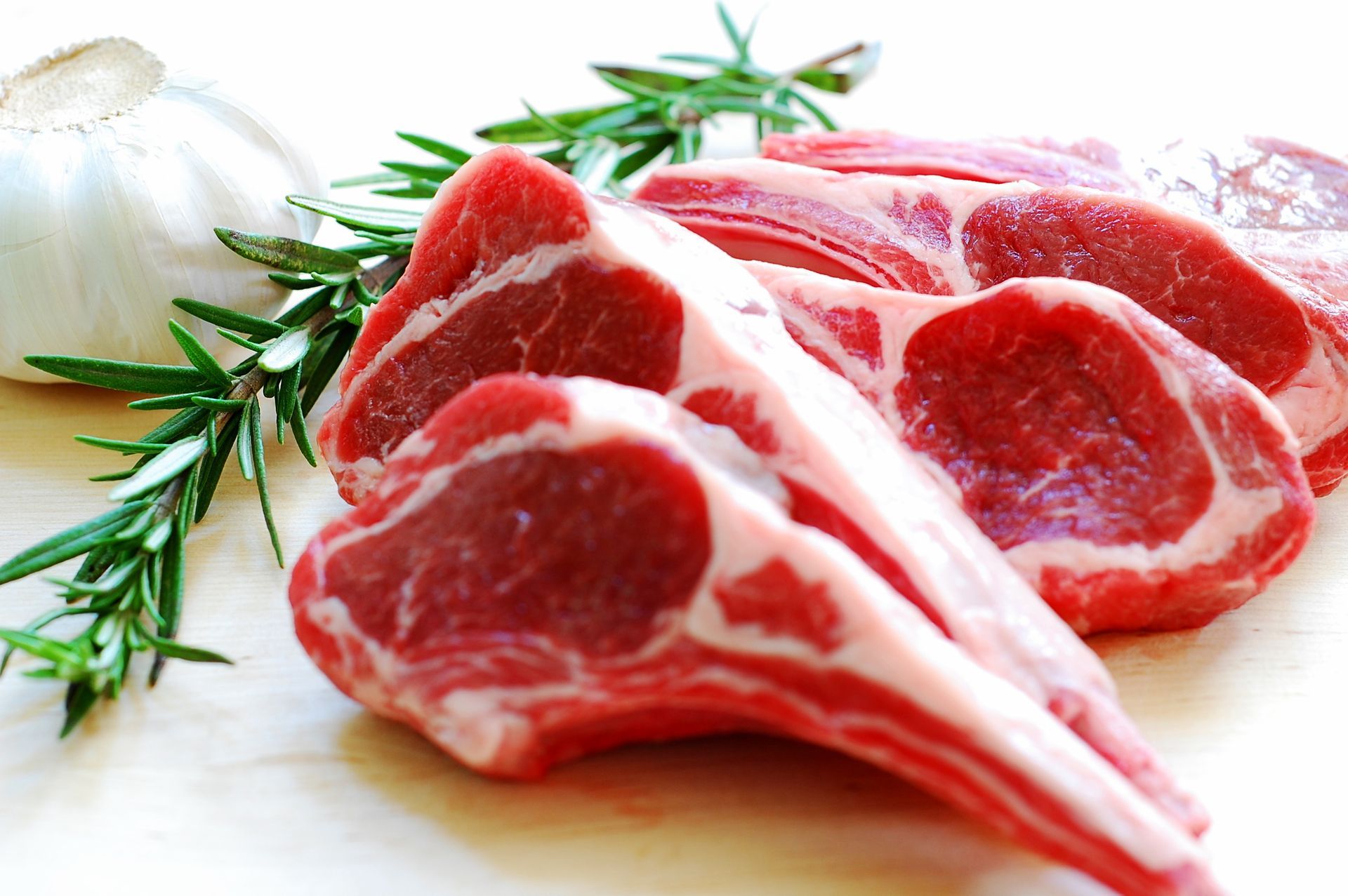 A pile of raw lamb chops next to garlic and rosemary