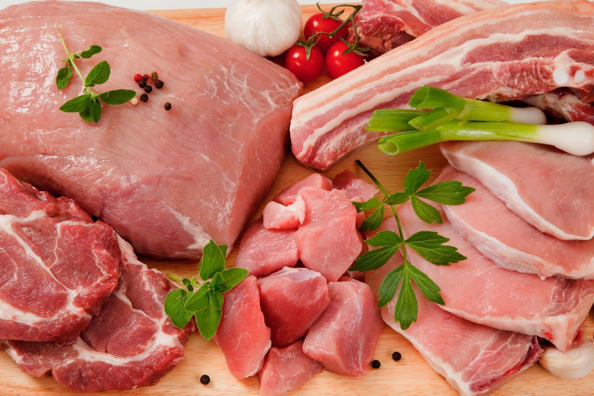 A variety of raw meats are on a wooden cutting board.