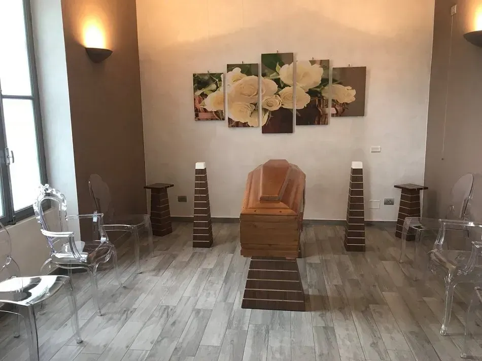 Interno di un'agenzia di pompe funebri con bara, arte floreale e sedie.
