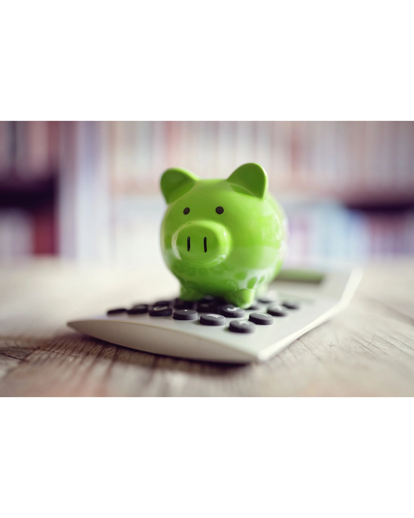 A green piggy bank is sitting on top of a calculator.