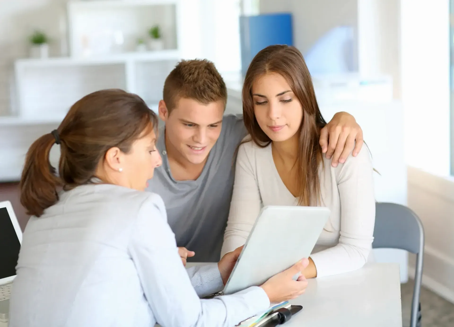 A man and a woman are sitting at a table looking at a tablet.