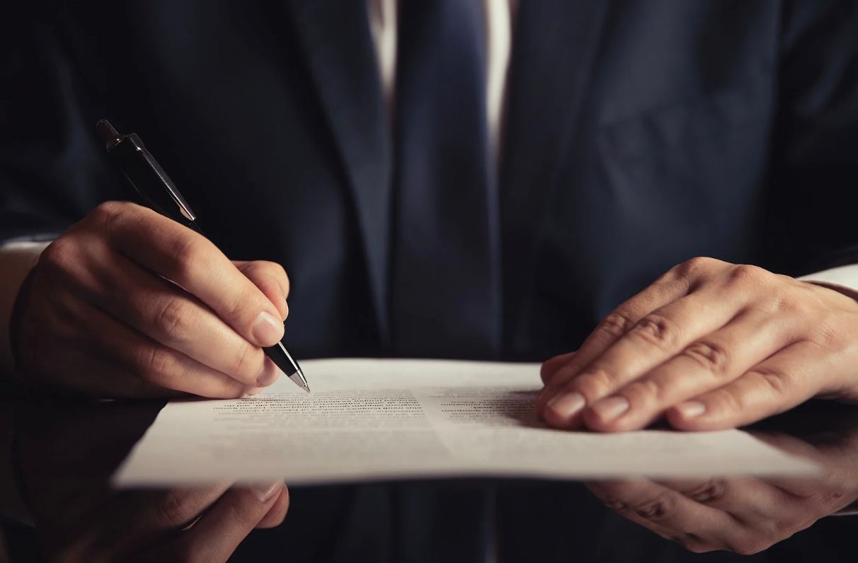 Man in suit writing on a document with a pen.