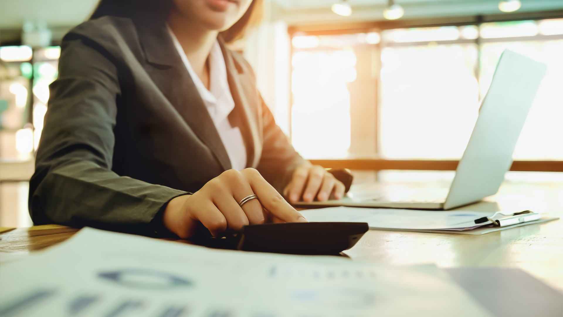 Woman in business suit using calculator with laptop and financial documents.