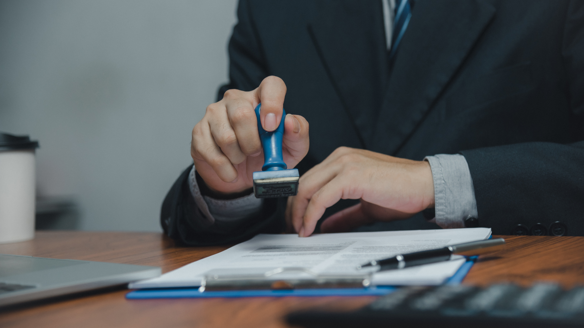 Person in suit stamping document with blue stamp at a desk.