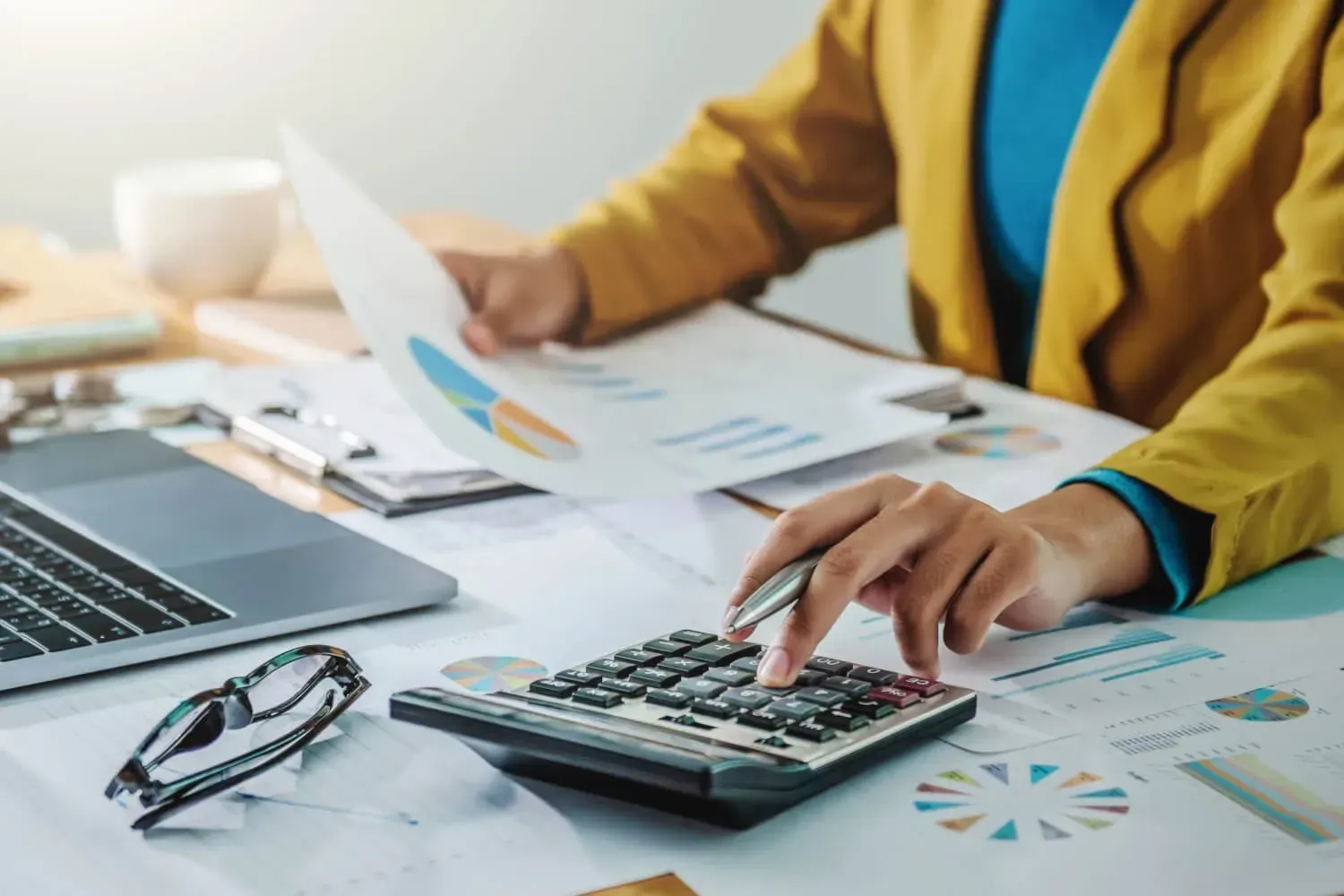 A woman is sitting at a desk using a calculator.