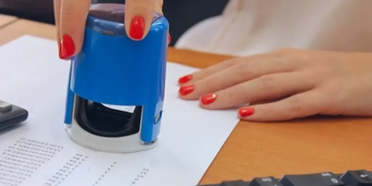 A woman is using a blue stamp on a piece of paper.
