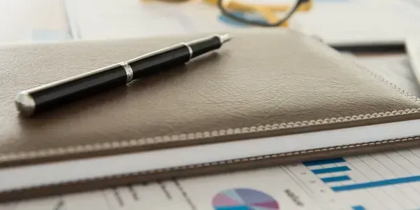 A pen is sitting on top of a notebook on a table.