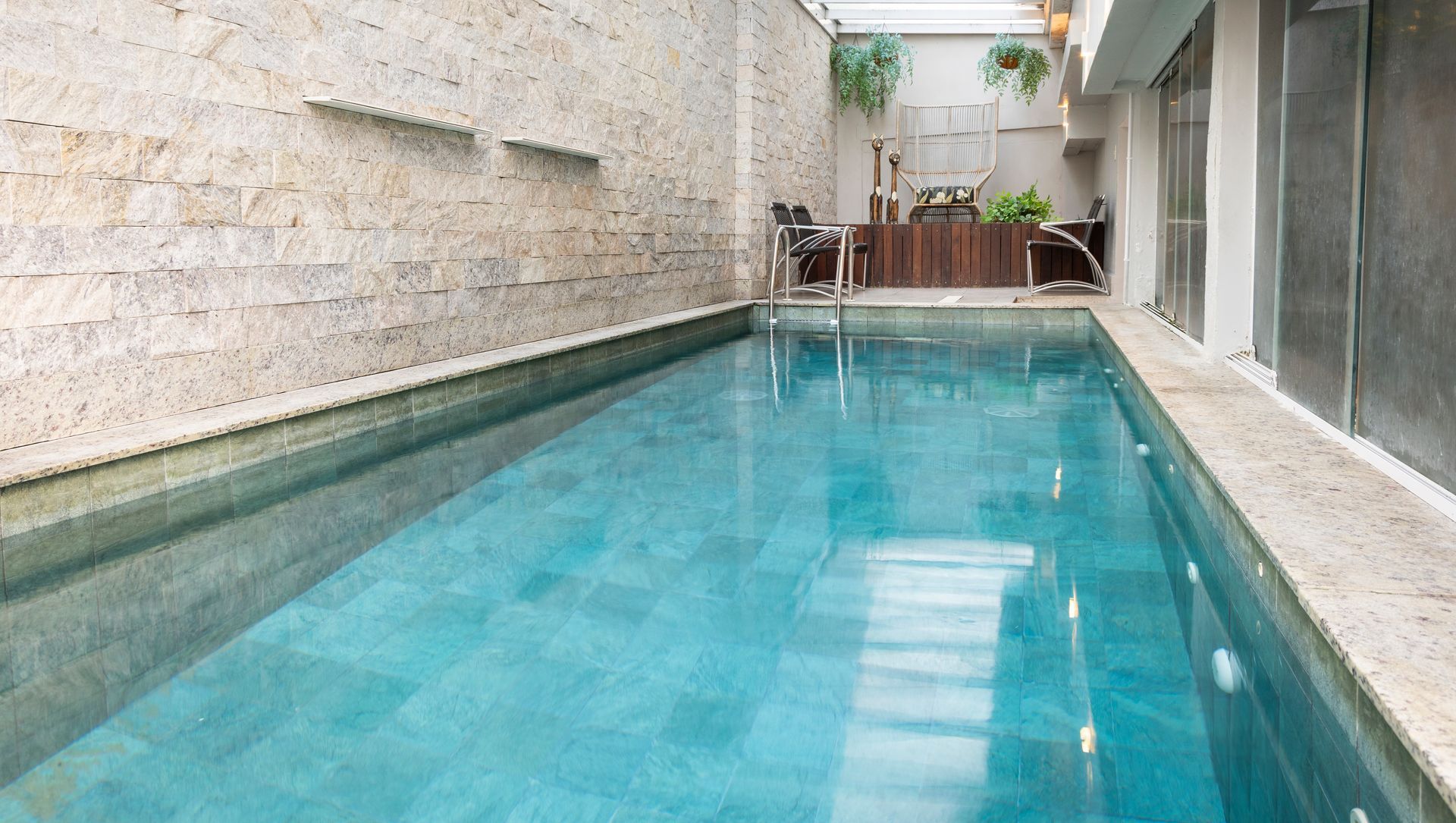 Piscina estreita coberta com água turquesa, paredes de pedra e espreguiçadeiras na extremidade oposta.