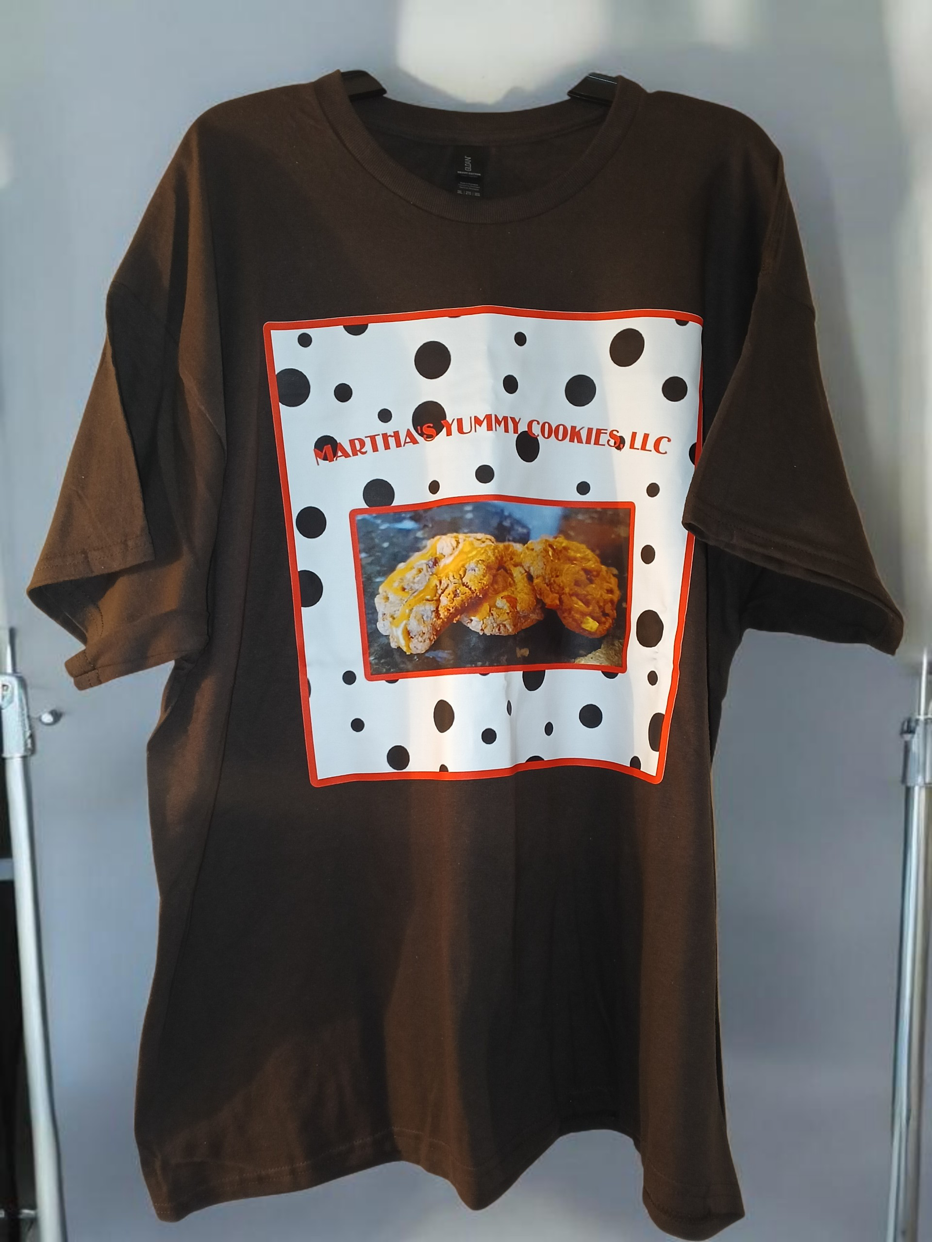 Brown t-shirt with a white square graphic featuring black polka dots, red text, and an image of fried food.