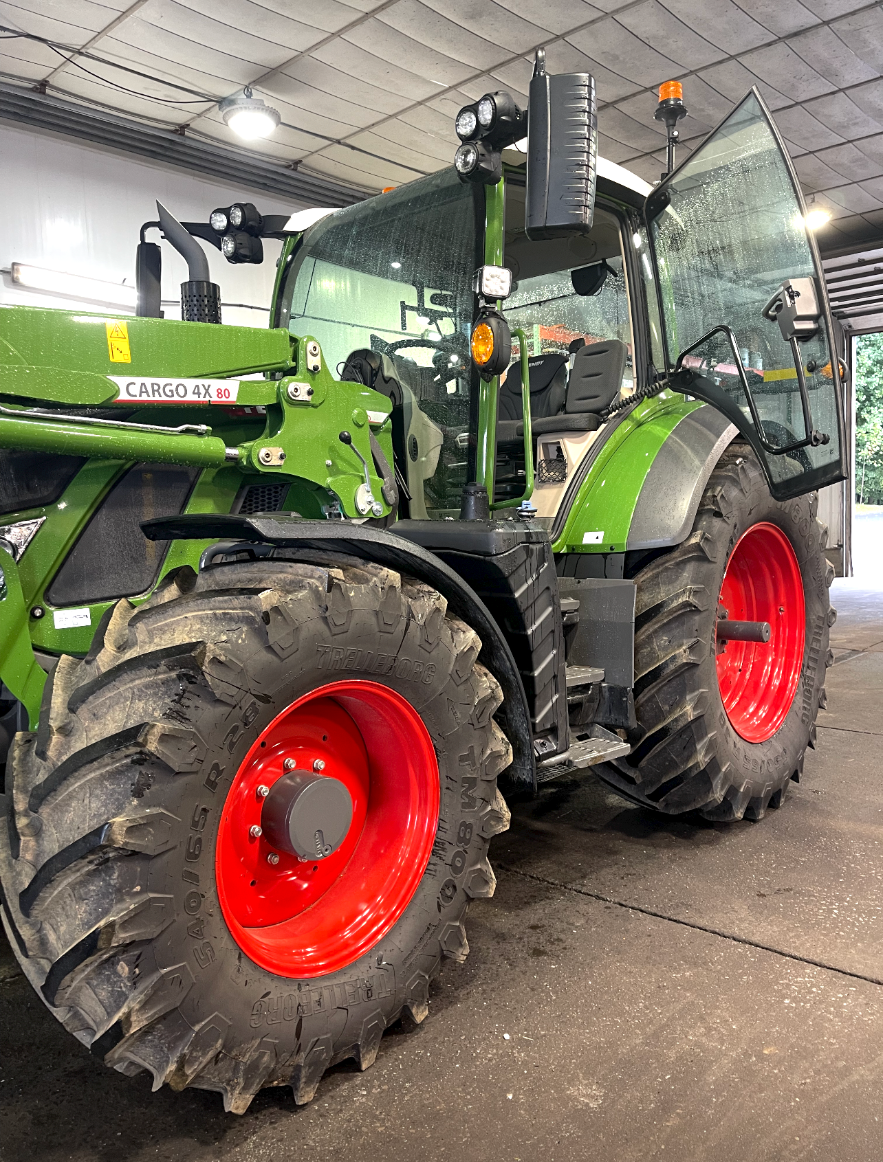 a green tractor with red wheels is parked in a garage .