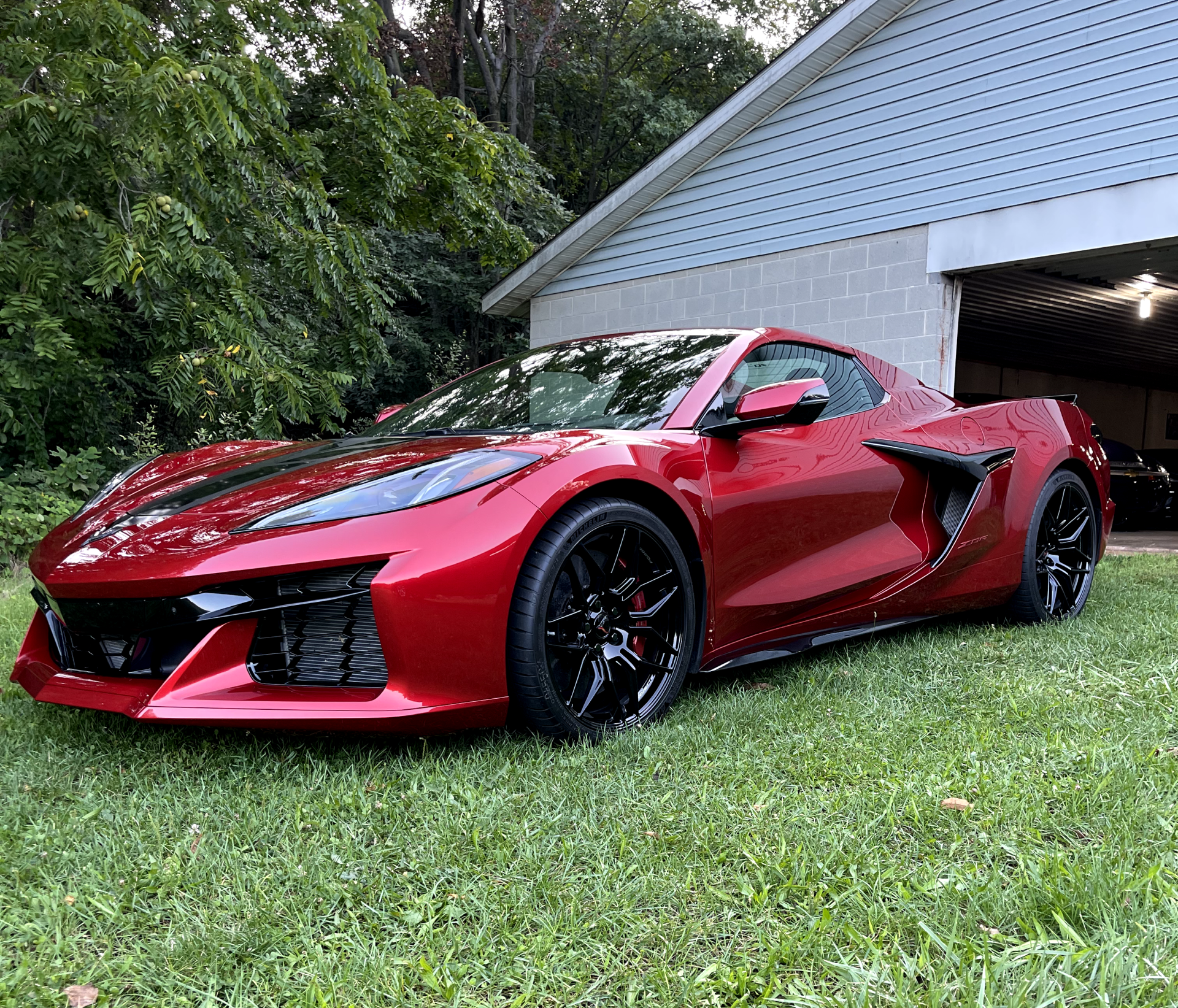 a red sports car is parked in the grass in front of a garage .