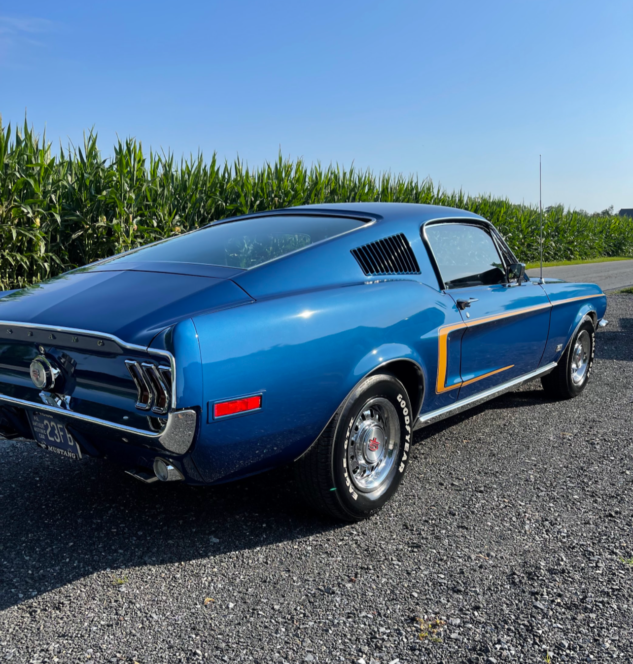 a blue mustang is parked in a gravel lot
