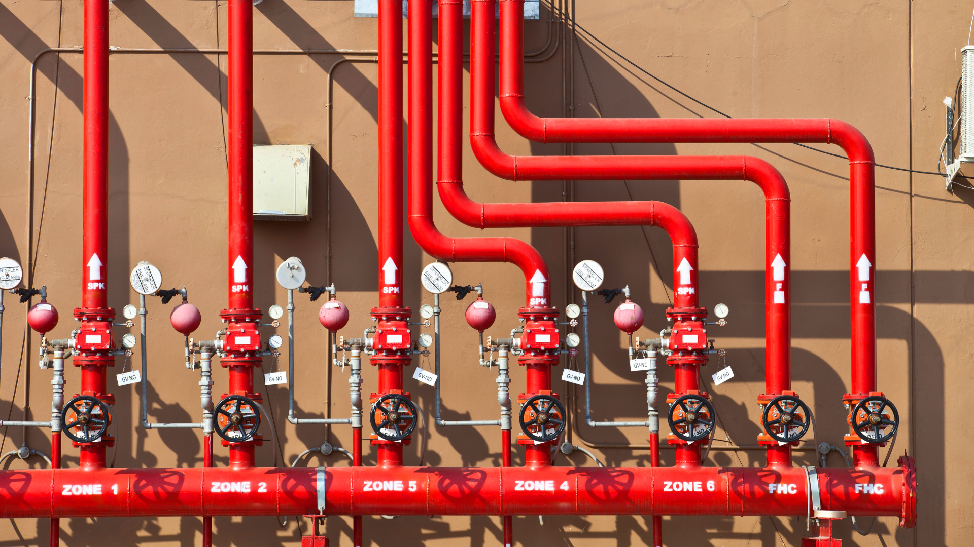A row of red pipes and valves on a wall.