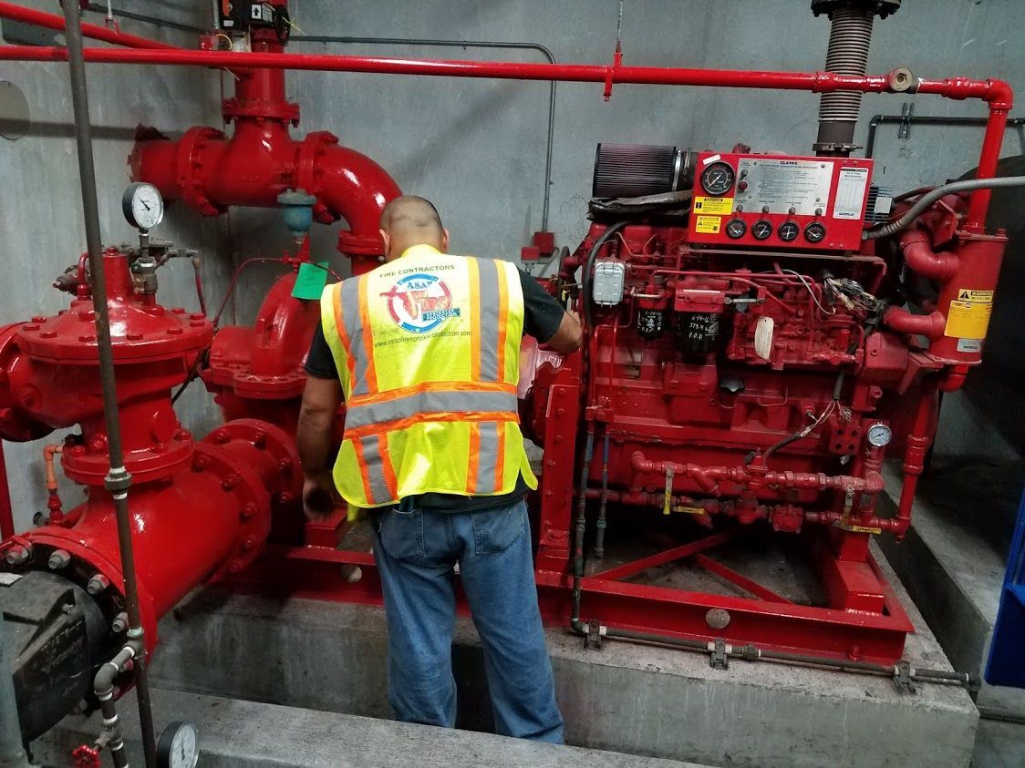 A man in a yellow vest is working on a red engine.