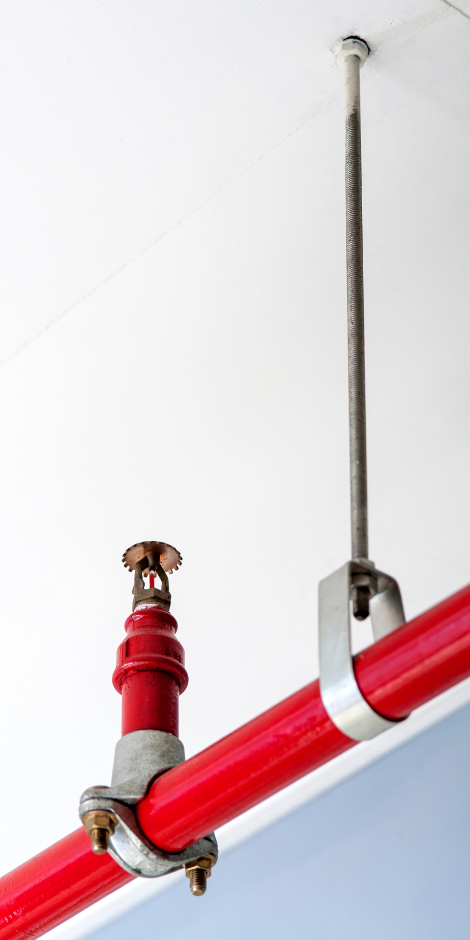 A red pipe with a sprinkler attached to it is hanging from the ceiling.