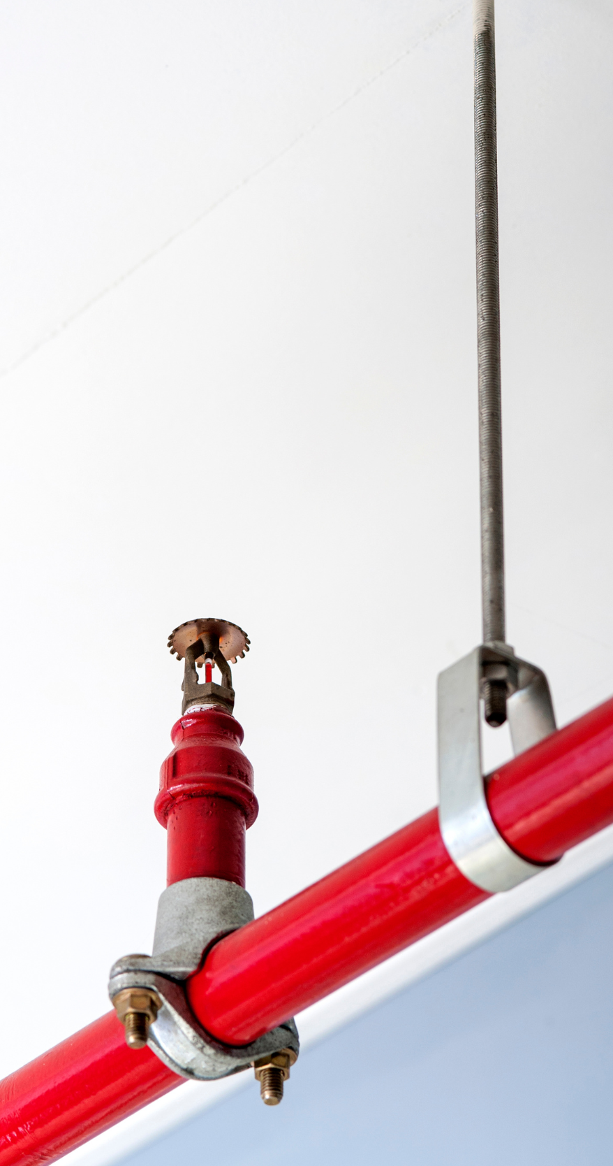 A red pipe with a sprinkler attached to it is hanging from the ceiling.