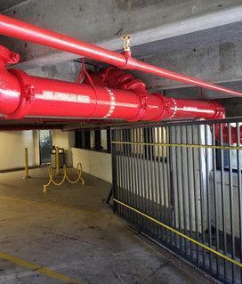 A red pipe is hanging from the ceiling of a parking garage.