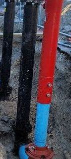 A red and blue pipe is sitting in the dirt next to a black pipe.