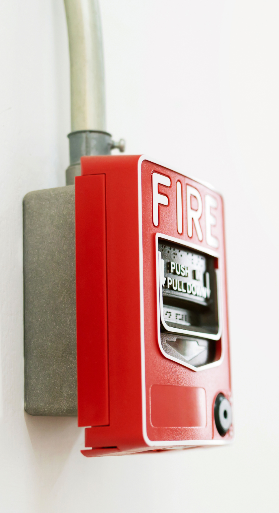 A red fire alarm is hanging on a white wall.