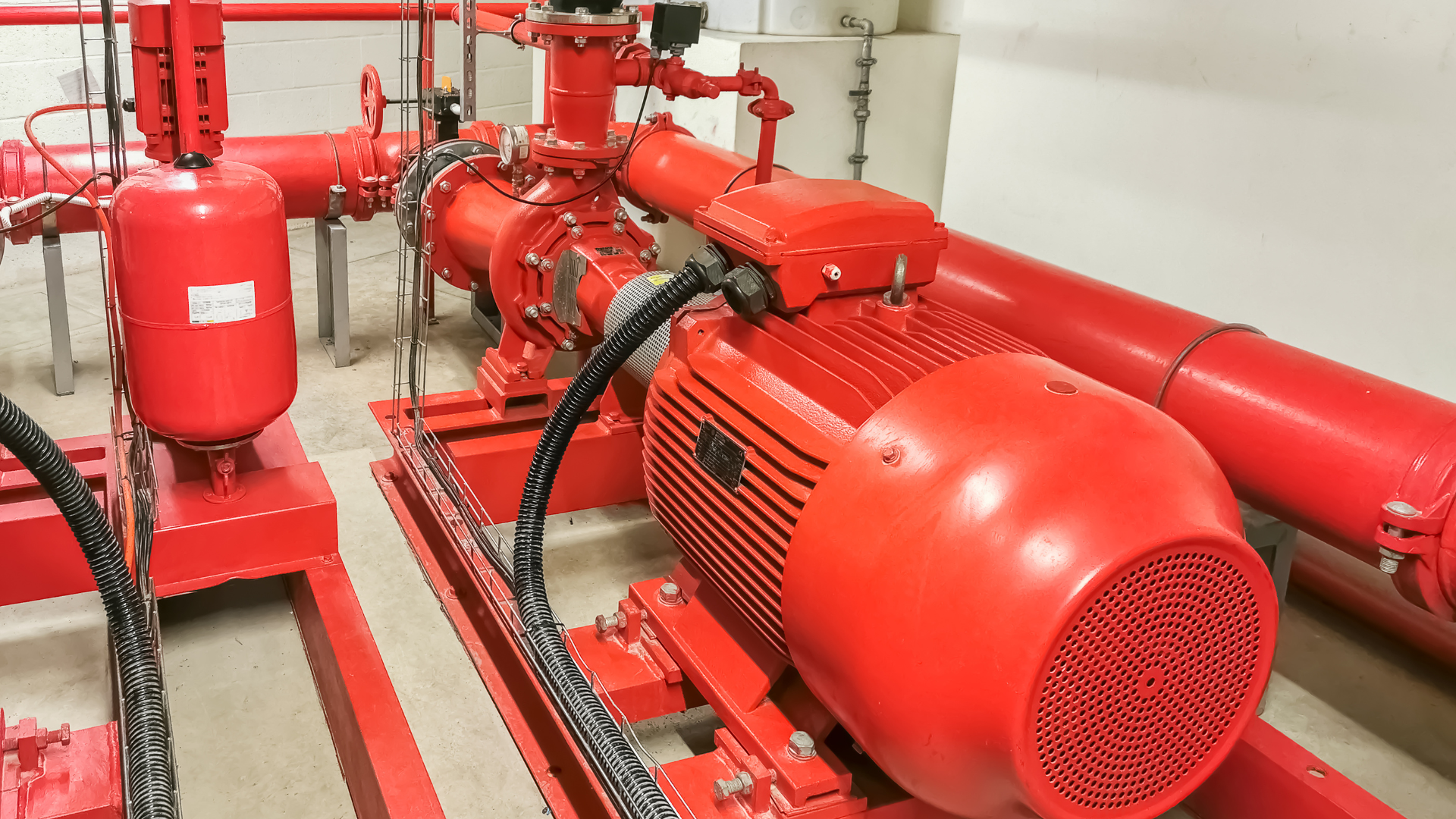 A red motor is sitting in a room surrounded by red pipes.